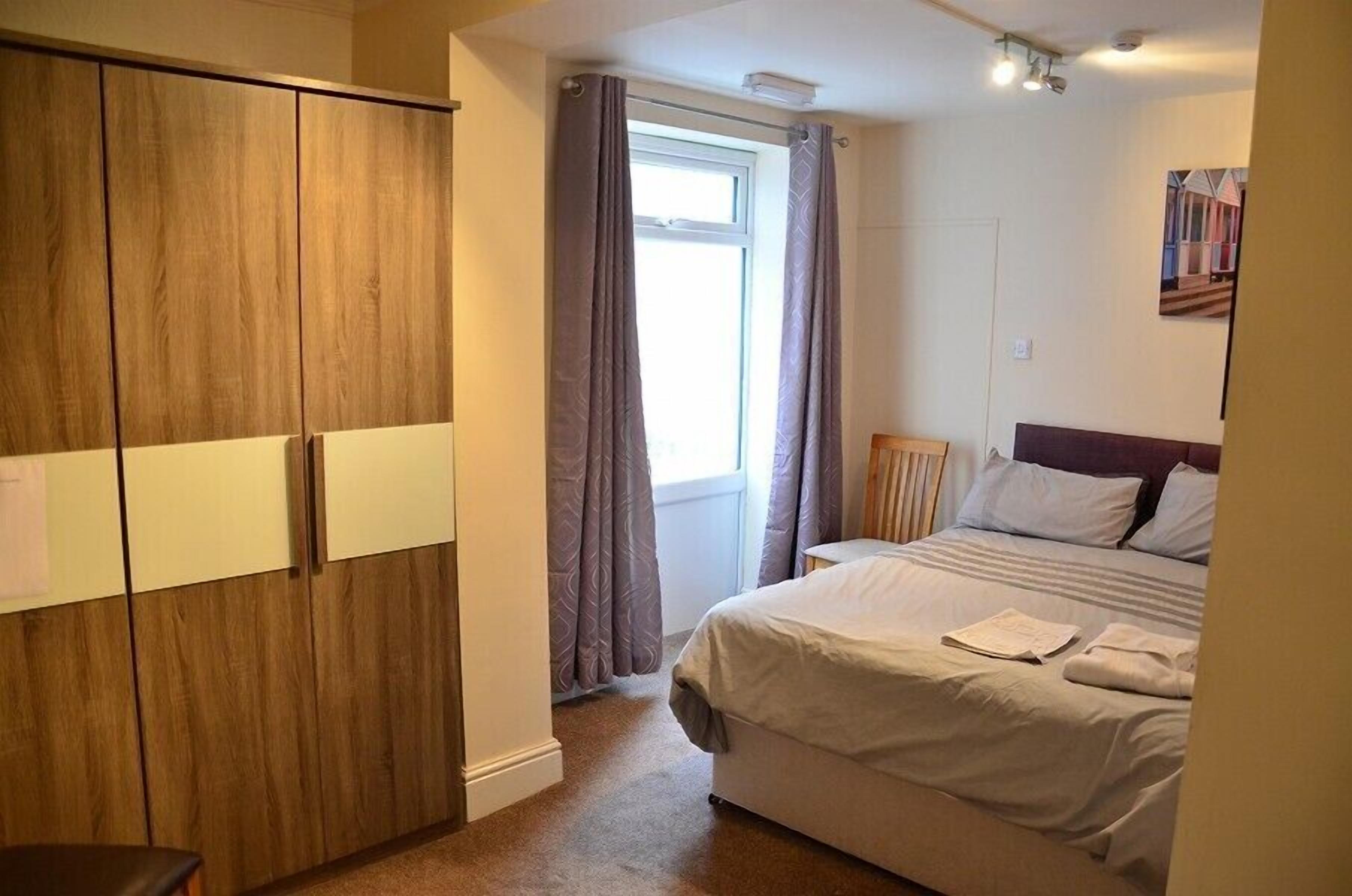 A bedroom with a bed, a wardrobe, and a window with curtains.