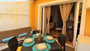 A dining area with a table set for four, a sofa with blue cushions, and a view through a glass door to a kitchen and living area. - Luxurious apartment with all comforts - 3 swimming pools - sunshine all day (adeje)