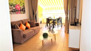 A living room with a sofa, a round table, and a dining area with chairs. - Luxurious apartment with all comforts - 3 swimming pools - sunshine all day (adeje)