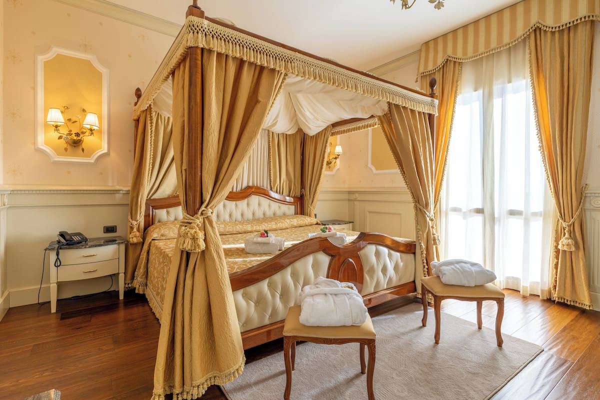 Un lit à baldaquin, une table de chevet avec une lampe et un petit banc avec des serviettes.