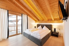 A bedroom with a wooden ceiling, a bed with white bedding, a nightstand with a lamp, and a view of a balcony. - Mountains Chalets (Seefeld in Tirol)