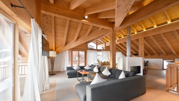A spacious living area with a large gray sofa, multiple white cushions, and a wooden ceiling. - Mountains Chalets (Seefeld in Tirol)