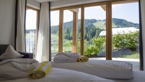 A hotel room with a large window offering a view of a green landscape and a distant building. - Mountains Chalets (Seefeld in Tirol)