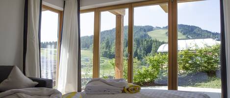 A hotel room with a large window offering a view of a green landscape and a distant building.