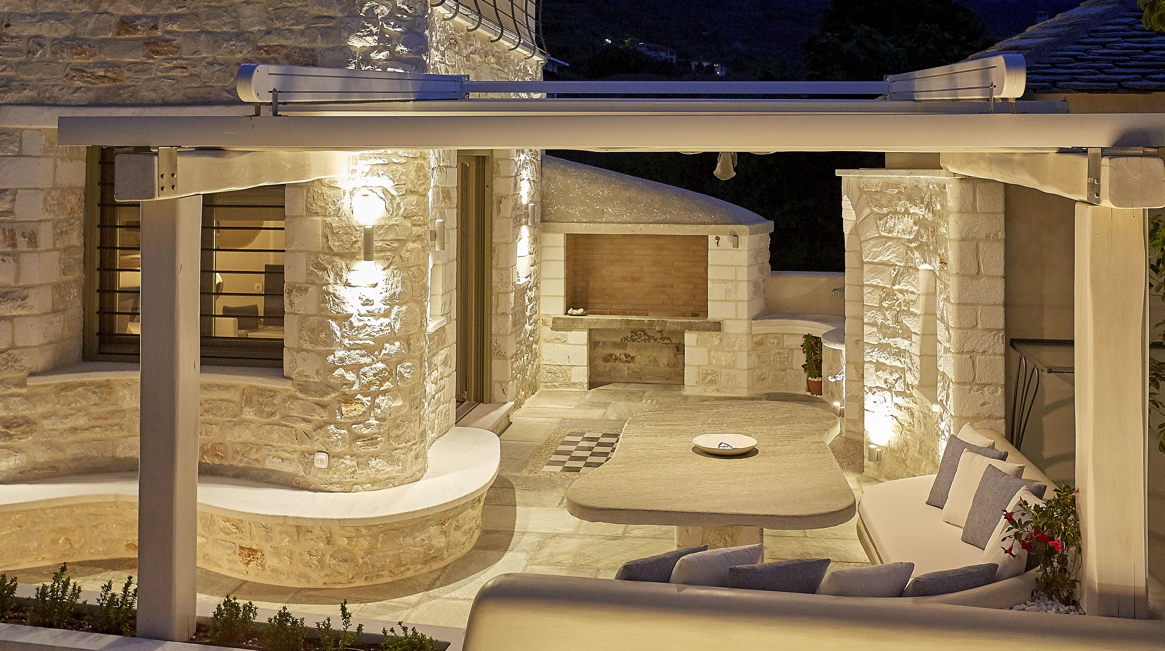 An outdoor patio with stone walls, a round table, and a built-in fireplace.