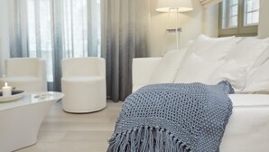 Una sala de estar moderna con un sofá blanco, un sillón redondo blanco, una mesita pequeña con una vela y una lámpara de pie.
