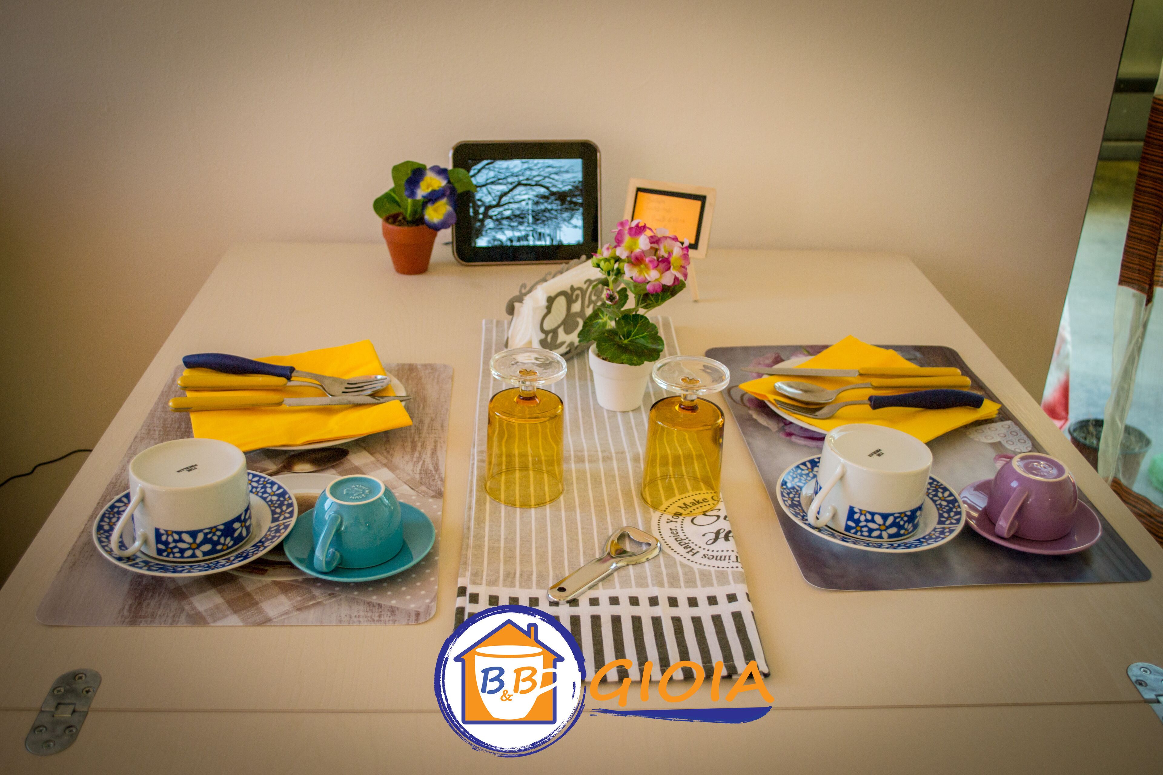 Une table dressée avec différentes tasses, soucoupes et serviettes, ainsi qu’une tablette et une petite plante en pot.