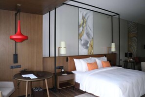 Une chambre d’hôtel avec un grand lit, une table de chevet, un bureau, une lampe suspendue rouge et des œuvres d’art accrochées aux murs.