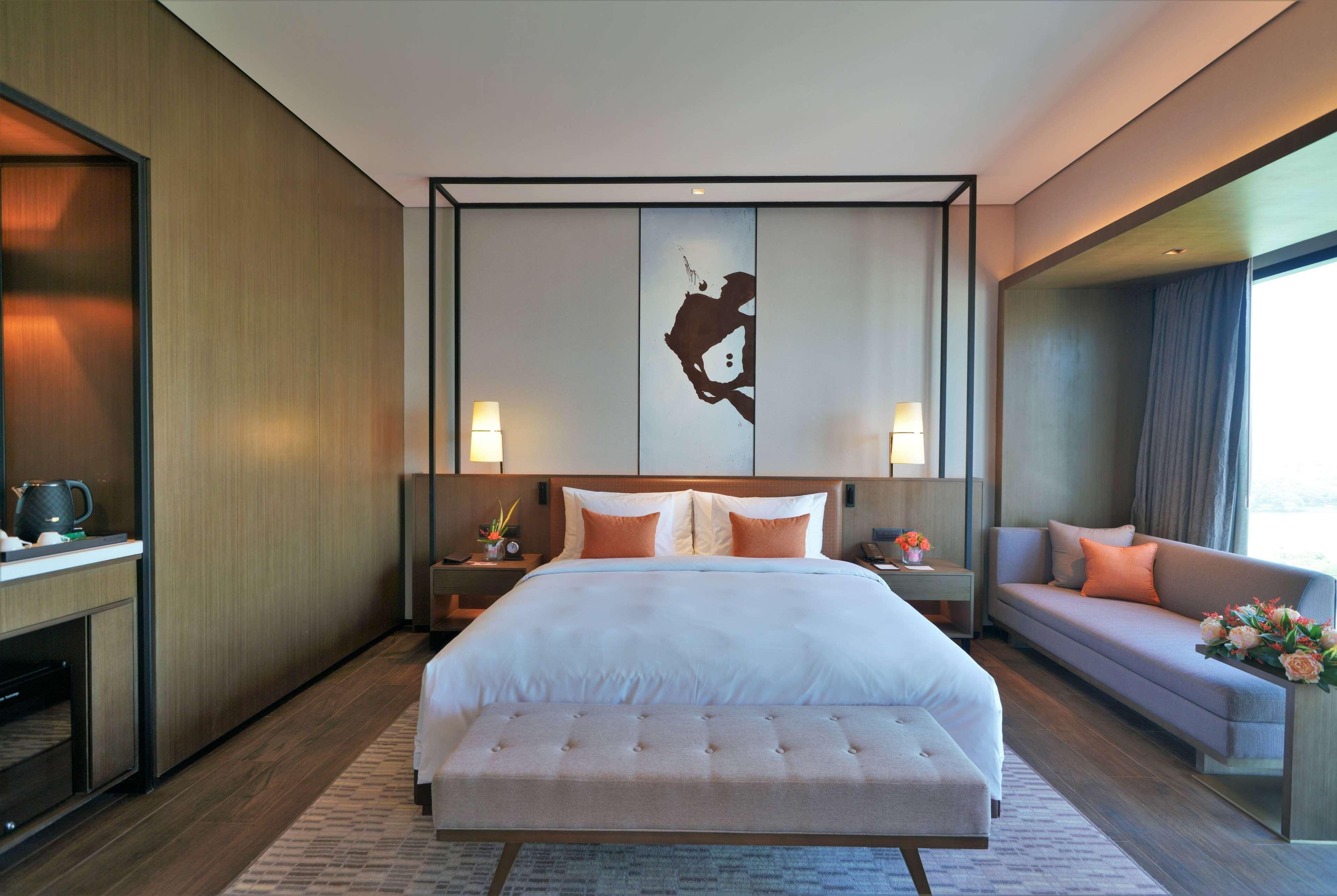 Una moderna camera d'albergo con un letto grande, un divano, un'opera d'arte appesa al muro e un comodino con una lampada.