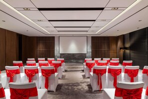 Un salón de conferencias con filas de sillas blancas con cintas rojas, una pantalla grande al frente y un diseño moderno del techo.