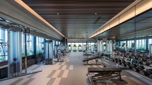 Un gimnasio con diversos equipos de ejercicio, ventanas amplias y suelo a cuadros.