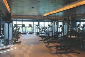 Une salle de sport équipée de tapis de course, d’appareils de musculation et de bancs.