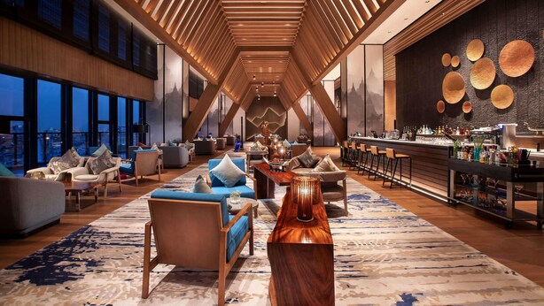 Un moderno vestíbulo de hotel con techos altos, listones de madera y una zona de bar con taburetes.