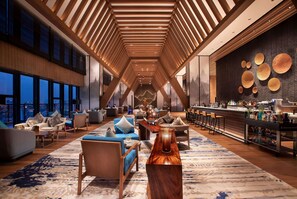 A spacious lounge area with a high ceiling, modern furniture, and a bar area with a variety of bottles. - Wyndham Grand Yangon (Yangon)