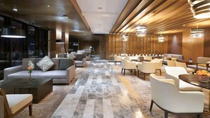 En moderne hotellobby med forskellige siddeområder, herunder sofaer og lænestole, et gulv med marmorlook og en væg beklædt med træpaneler.