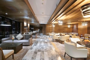 A modern hotel lobby with a marble floor, sofas, dining area, and wooden paneling. - Wyndham Grand Yangon (Yangon)