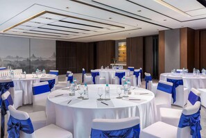 A conference room with round tables, white chairs with blue sashes, and a cityscape mural on the wall. - Wyndham Grand Yangon (Yangon)