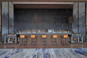 A bar area with a long counter, multiple stools, and a variety of bottles and glasses. - Wyndham Grand Yangon (Yangon)