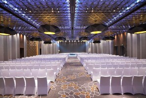 Un salón de conferencias con hileras de sillas blancas, una alfombra estampada y un diseño geométrico en el techo.