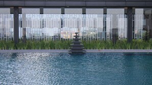 En swimmingpool med et trappetrinssystem af vandelementer i midten, omgivet af en moderne bygning med store vinduer og udsigt over bybilledet.
