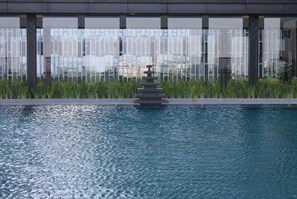 A swimming pool with a tiered water feature in the center, surrounded by a glass barrier and greenery. - Wyndham Grand Yangon (Yangon)