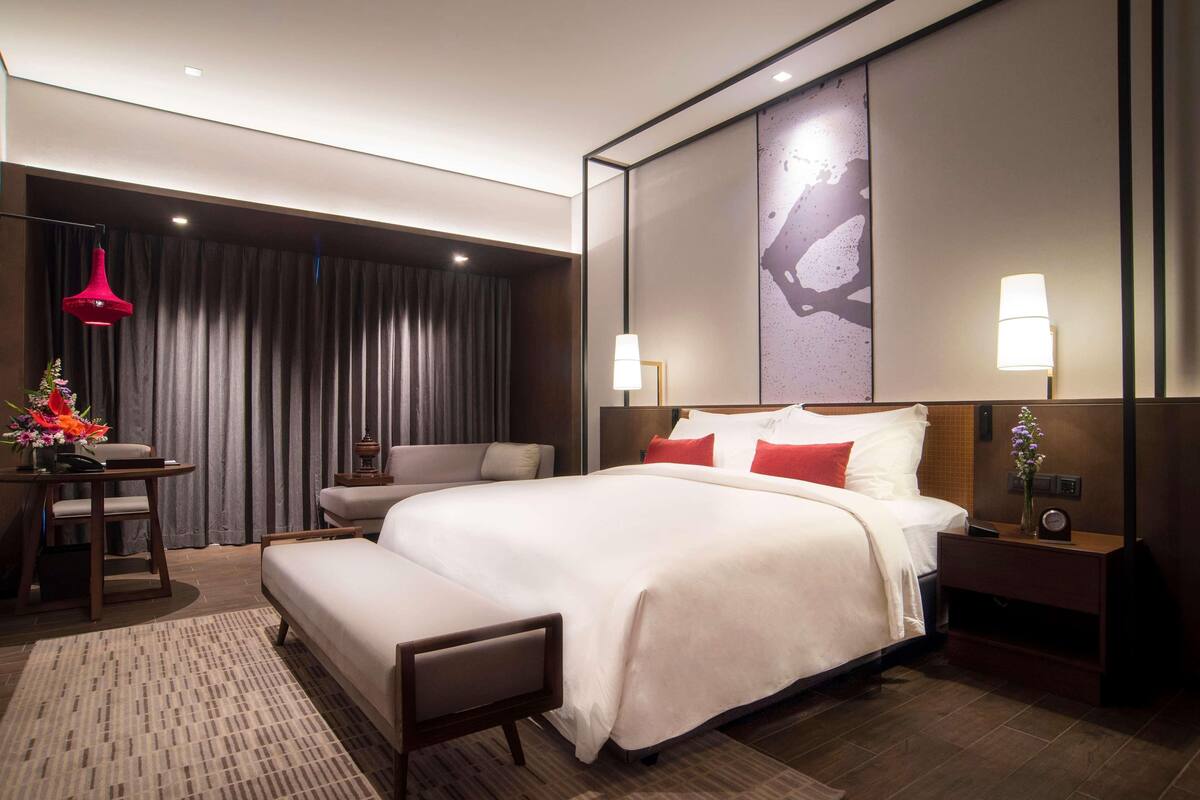 A modern hotel room with a large bed, bedside tables, a desk, and a chair.