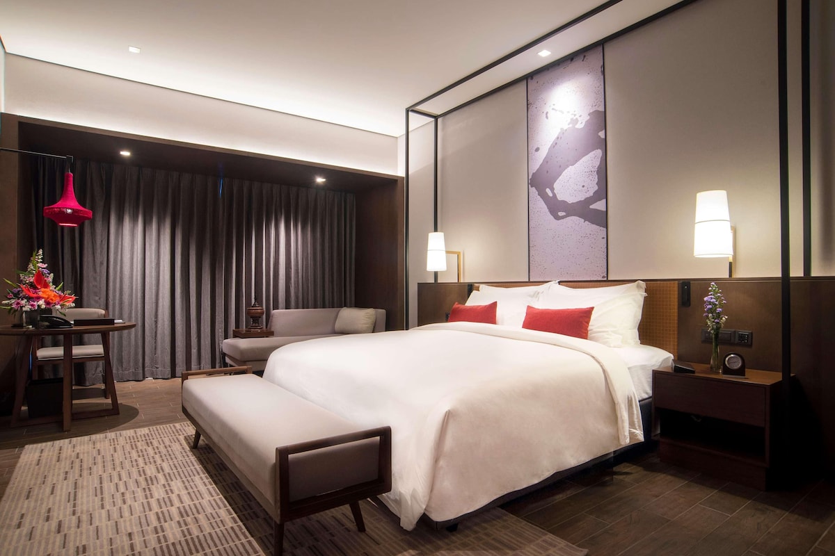 A modern hotel room with a large bed, bedside tables, a desk, and a chair.