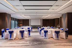 A conference room with round tables, white chairs with blue sashes, and a projector screen. - Wyndham Grand Yangon (Yangon)
