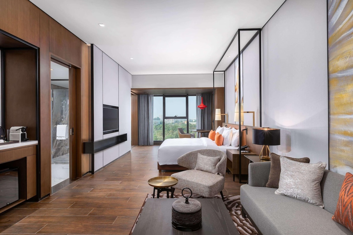 A modern hotel room with a large bed, a sofa, a coffee table, and a TV.