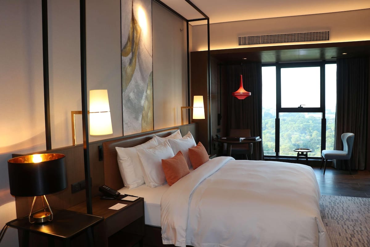 Quarto de hotel com uma cama grande, abajures, vista para o exterior e uma pequena mesa com uma cadeira.