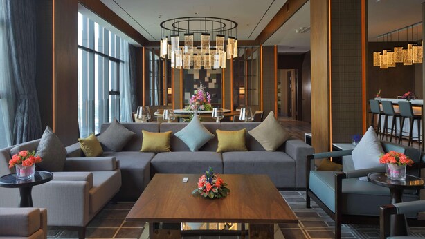 En moderne hotellobby med en stor sofa, lænestole, et sofabord og et spiseområde i baggrunden.