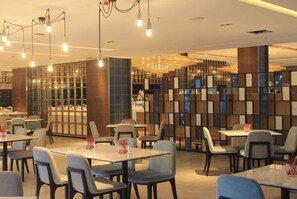 L’intérieur d’un restaurant moderne, avec des tables, des chaises et un mur décoratif orné de motifs géométriques.