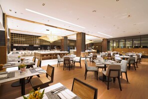 Un restaurante moderno con varias zonas de comedor, una barra central y una cocina visible al fondo.