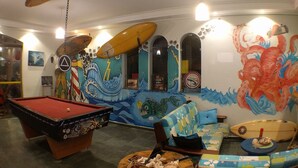 Una stanza con tavolo da biliardo, divano e un murale raffigurante tavole da surf e onde dell'oceano.