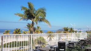 Una terrazza con tavoli e sedie, vista su una spiaggia e palme.