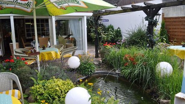 A restaurant with outdoor seating, a garden with a pond, and a large umbrella. - Bei Hölzchen (Hannover)