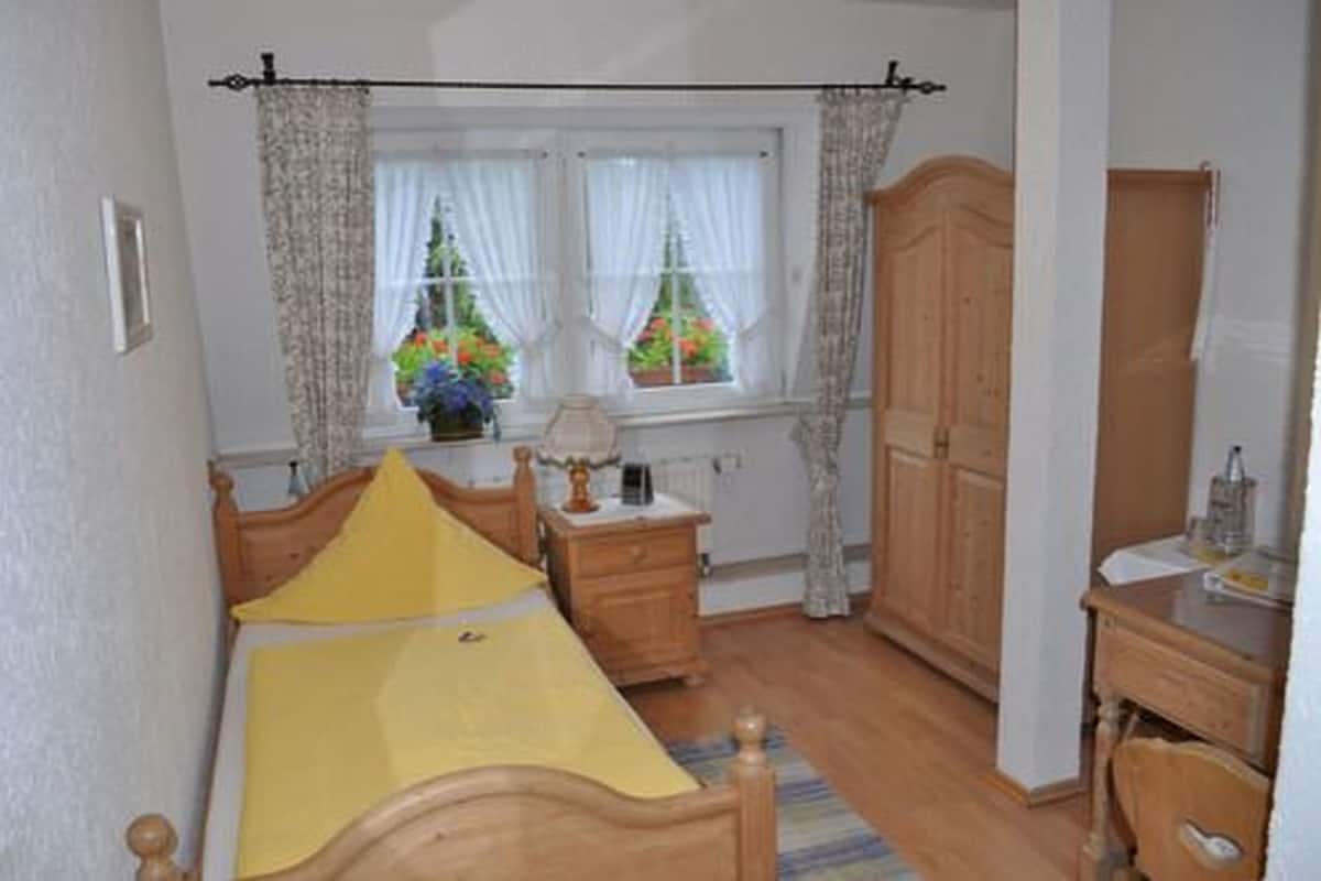 A bedroom with a bed, a nightstand, a dresser, and a window with curtains.