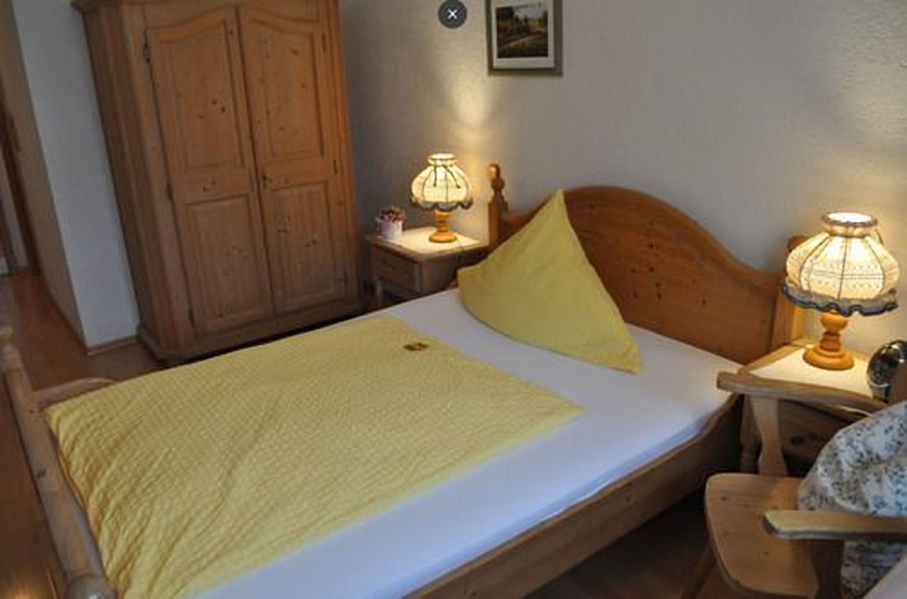 A bedroom with a wooden bed, two bedside lamps, a wooden wardrobe, and a small bedside table.