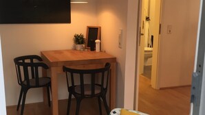 A cozy room with a wooden dining table, two chairs, a sofa with a patterned cover, and a painting on the wall. - Cozy and charmingly furnished 30sqm apartments in a central location in Husum (Husum)