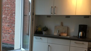 A compact kitchen with white cabinets, a coffee maker, and a window overlooking a brick wall. - Cozy and charmingly furnished 30sqm apartments in a central location in Husum (Husum)