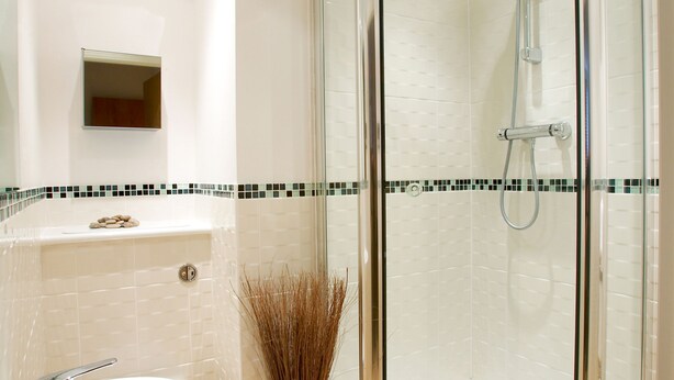 A modern bathroom with a glass-enclosed shower, a white sink, and a tiled backsplash. - Pelican House (Newbury)