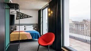 A hotel room with a bed, a red chair, a balcony with a view, and a sign on the wall. - The Social Hub Berlin (Berlin)
