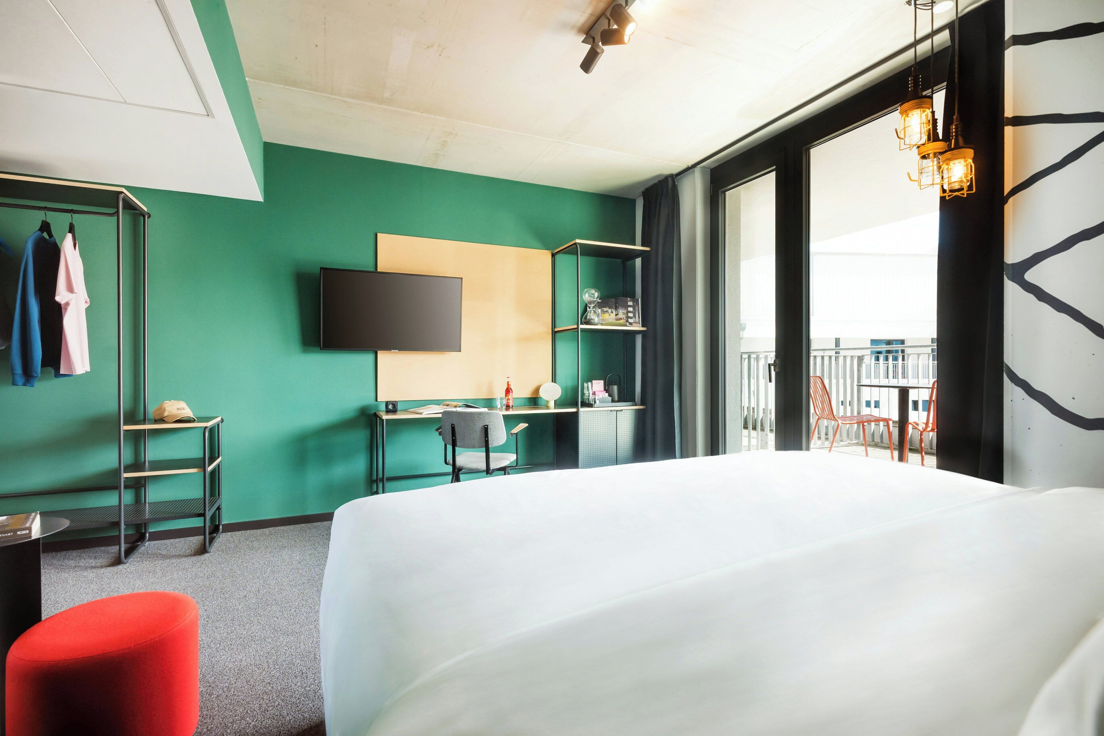 Una camera d'albergo con un letto, una scrivania, una televisione e un balcone con sedie.