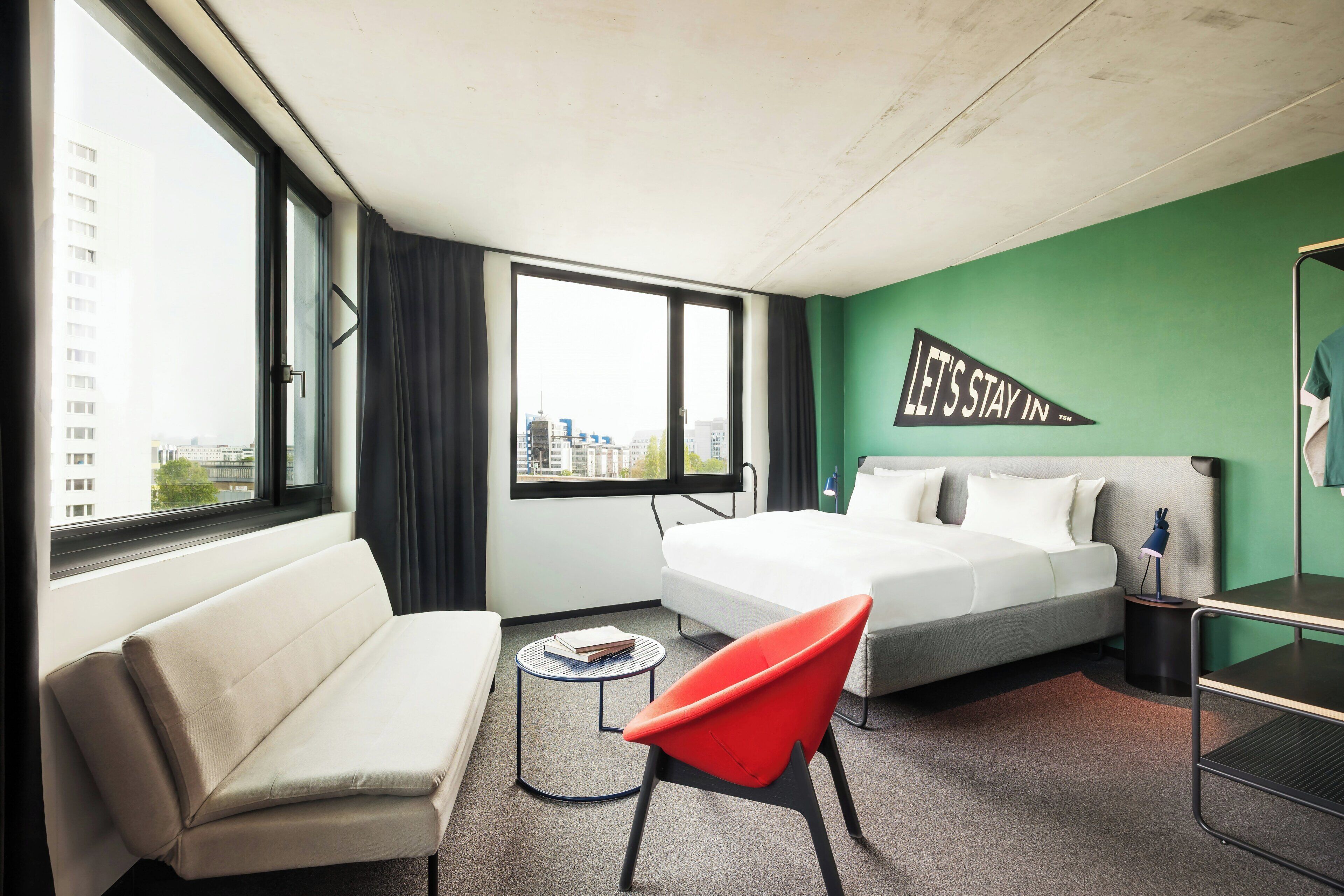 Een hotelkamer met twee bedden, een bank, een rode stoel, een kleine tafel en uitzicht over de stad.