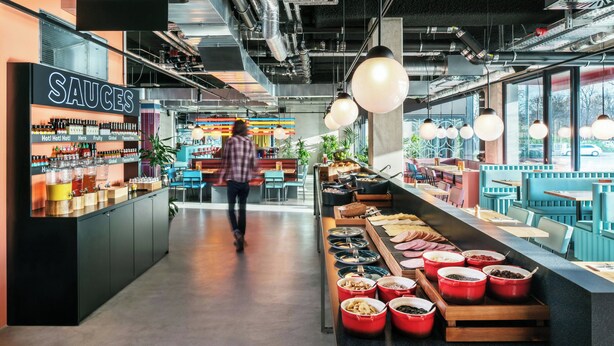 Un restaurante moderno con una barra central que exhibe diversos alimentos y salsas.