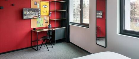Habitación de hotel con una pared de acento roja, un escritorio con silla, una cama, una ventana con vistas y un espejo.