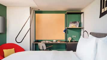 A hotel room with a bed, a desk with a chair, a television, and a green wall.