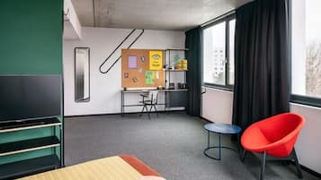 Ein Hotelzimmer mit Bett, Schreibtisch, Stuhl, Fernseher und einem Fenster mit Vorhängen.