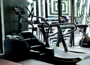 Ett gym med löpband och en motionscykel, med en betongvägg och fönster i bakgrunden.