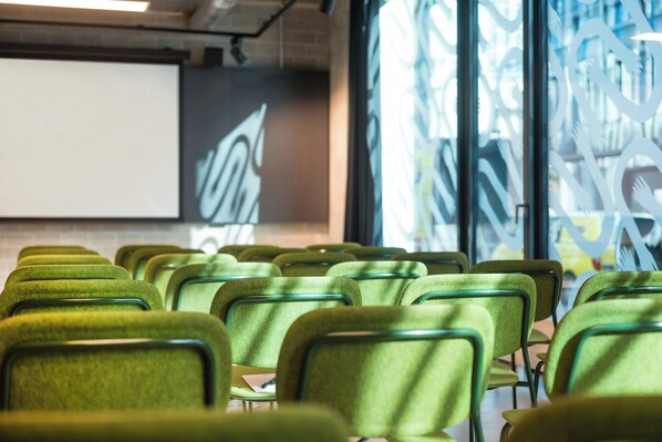 Rows of green chairs arranged in a conference room with a projector screen and abstract wall art. - The Social Hub Berlin (Berlin)